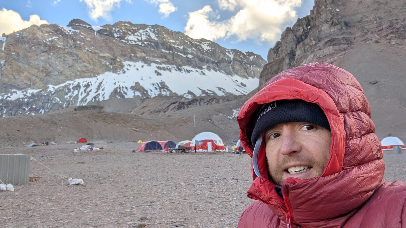 Aconcagua base camp: tents on the scree under the mountain wall, Sam in a red down hood in the foreground